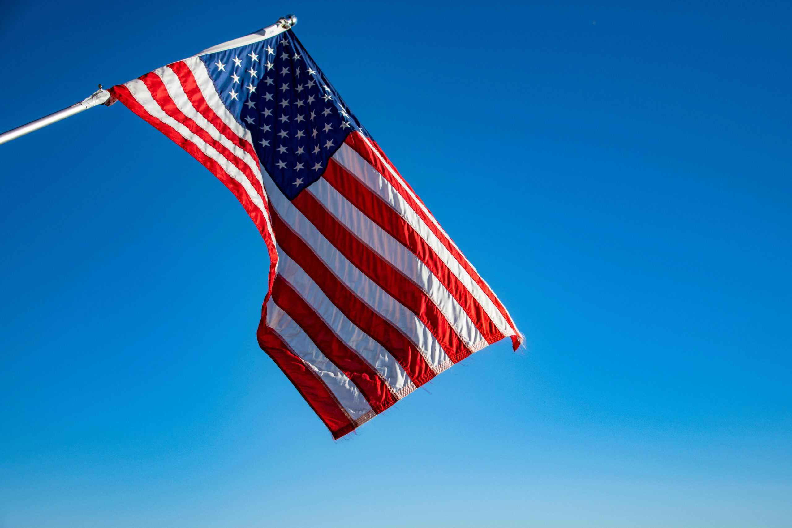 The American flag proudly waves on a flagpole against a clear blue sky, symbolizing freedom and patriotism.